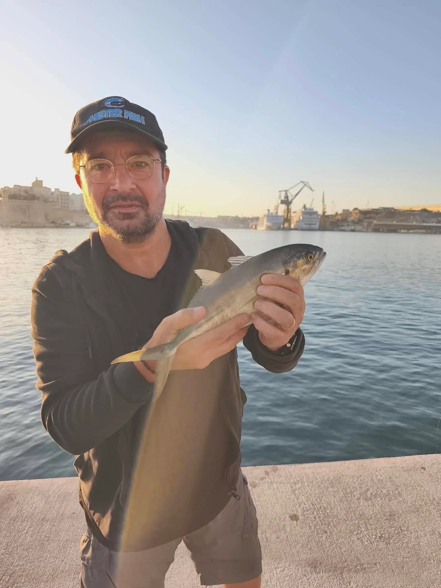 An angler holding a fish in the warm light beside the harbour