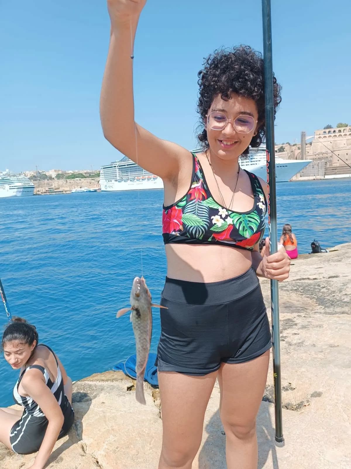 An angler with a fishing pole and catch beside the clear harbour water