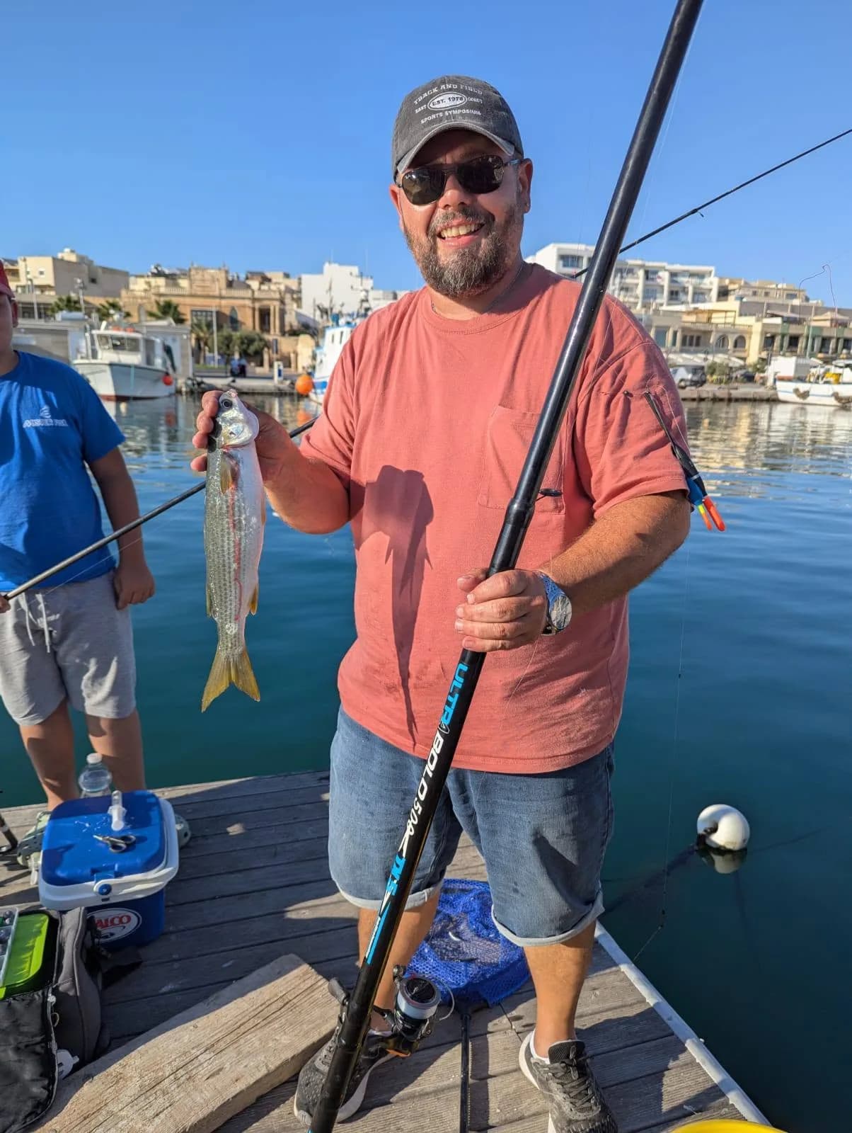 An angler holding a fishing pole and catch beside the harbour