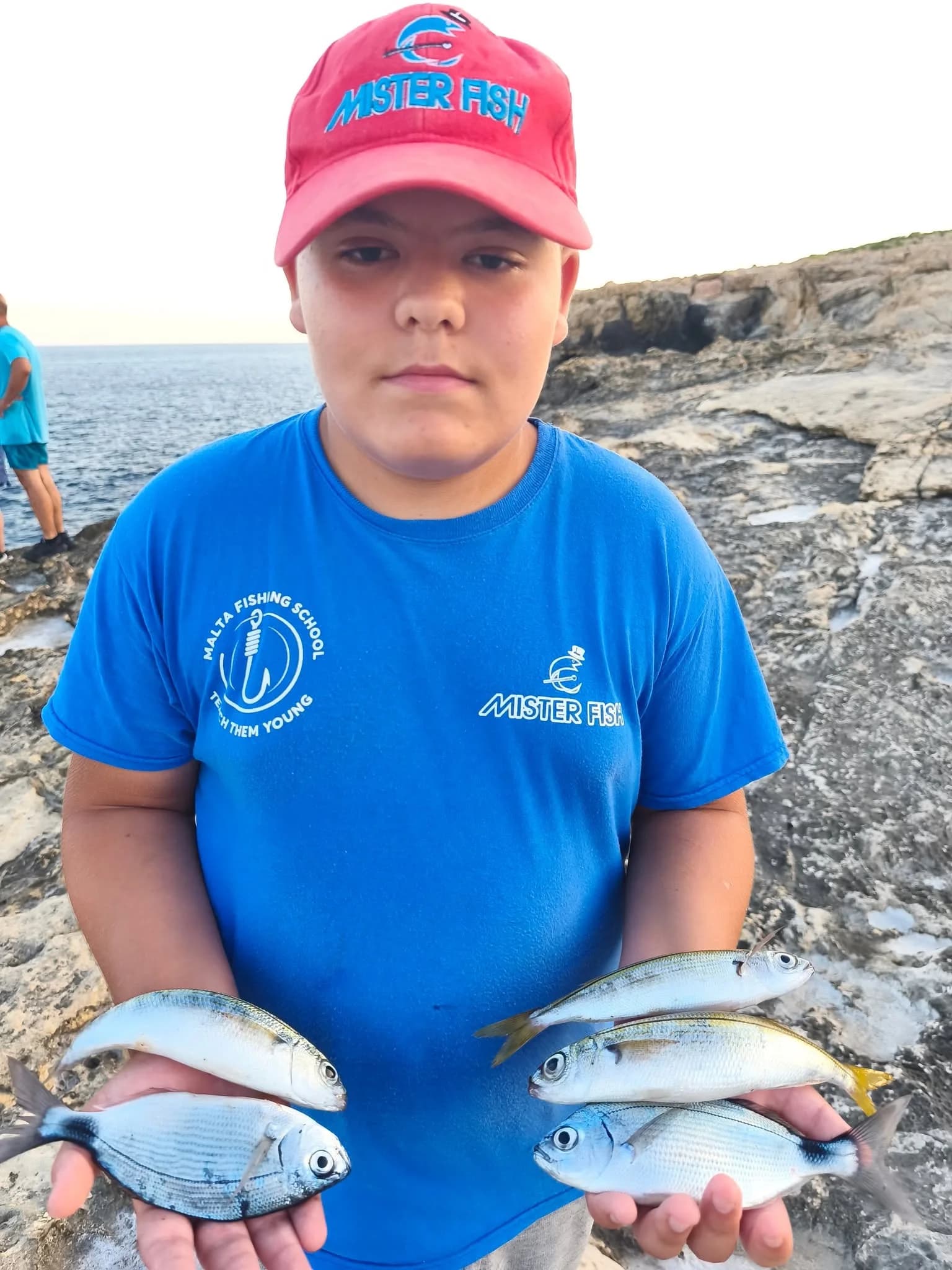 A young angler in a blue shirt holding two fish beside the water