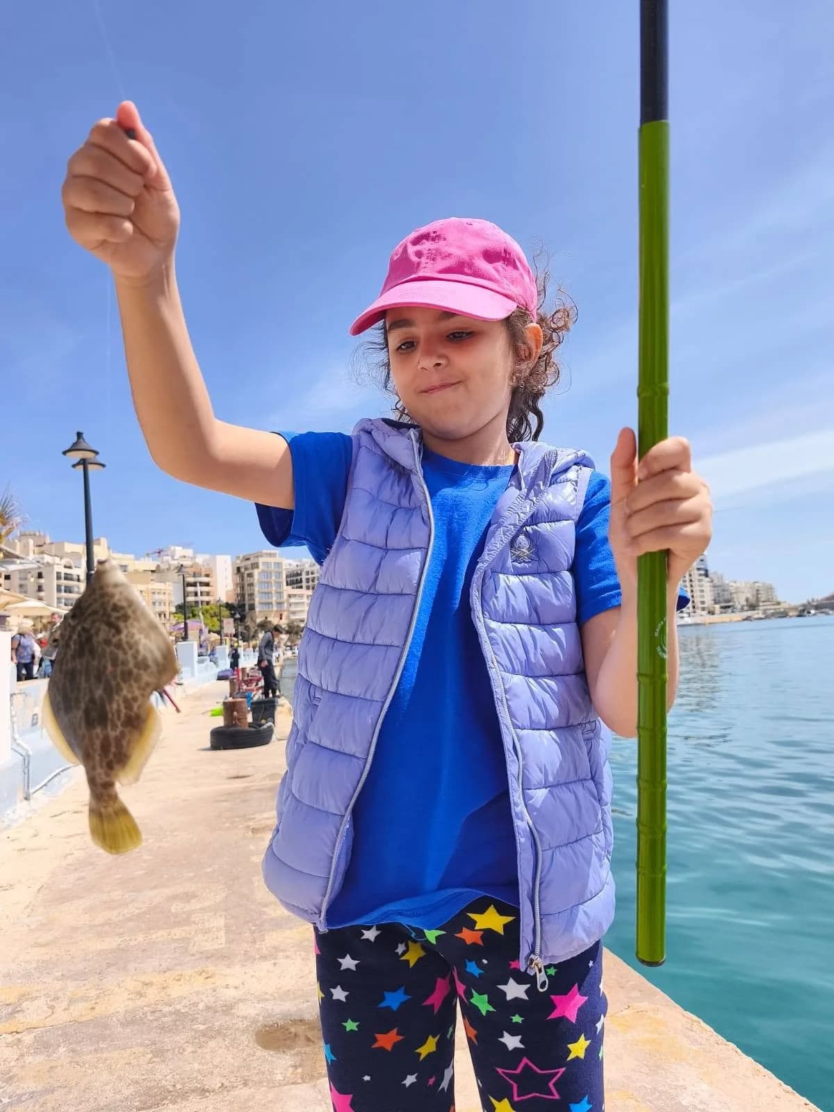 A smiling young angler in an orange shirt with a pole and catch